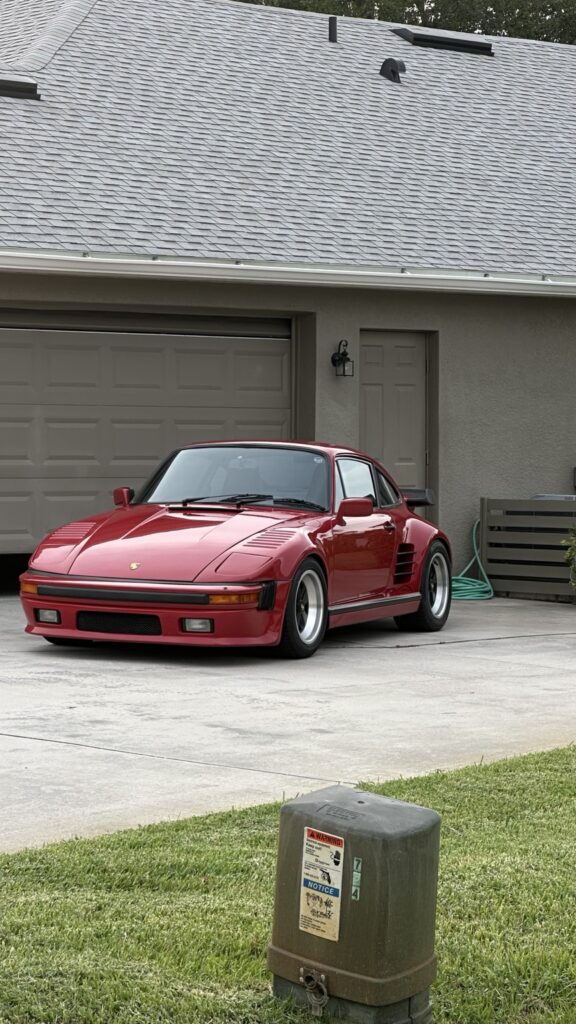 Red classic Porsche parked outside a garage